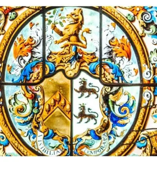 Colourful stained glass window featuring a crest with a lion on top, two lions inside a shield, swirling floral patterns, and the Latin motto Visibilia Temporaria.